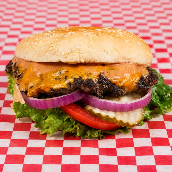 Cheeseburger with lettuce, tomato, red onion, and pickles on a red and white checkered paper.