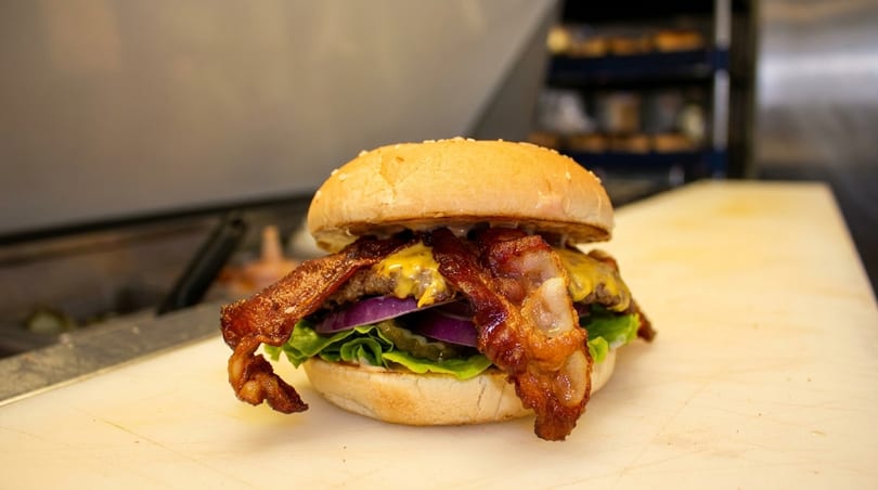 A bacon cheeseburger with lettuce, red onion, and pickles on a sesame seed bun.