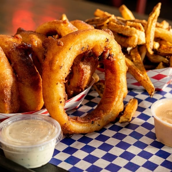 Crispy onion rings and golden french fries in checkered paper boats with dipping sauces.