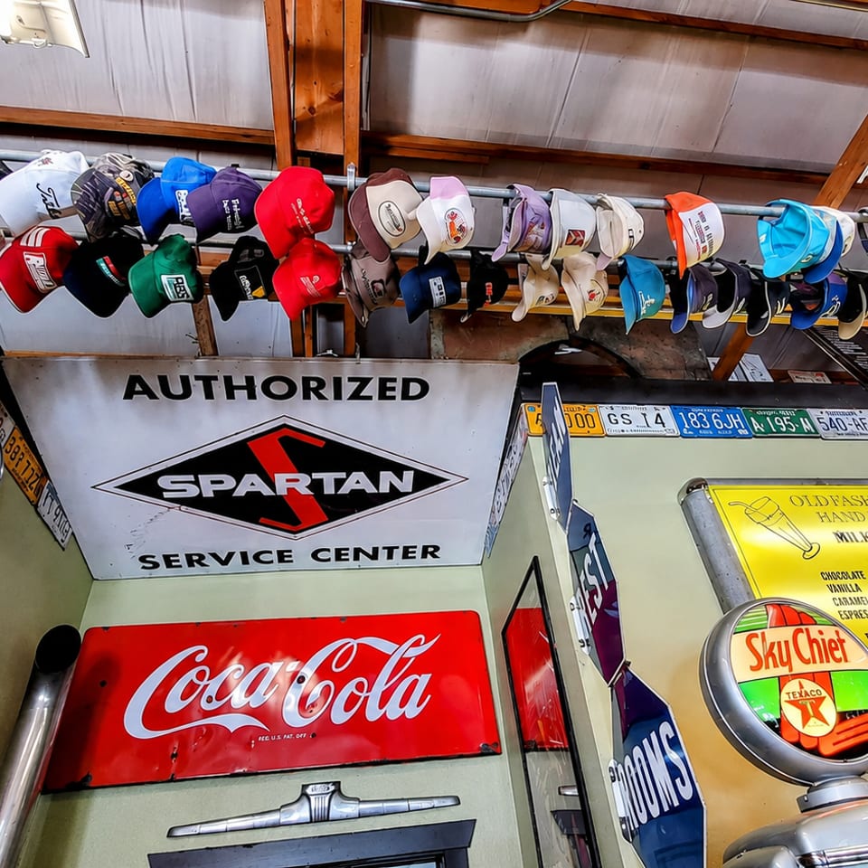 A wall decorated with vintage signs, license plates, hubcaps, and a row of colorful hats.