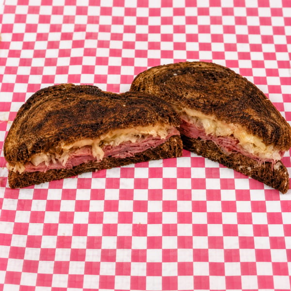 A reuben sandwich, cut in half, on red and white checkered paper.